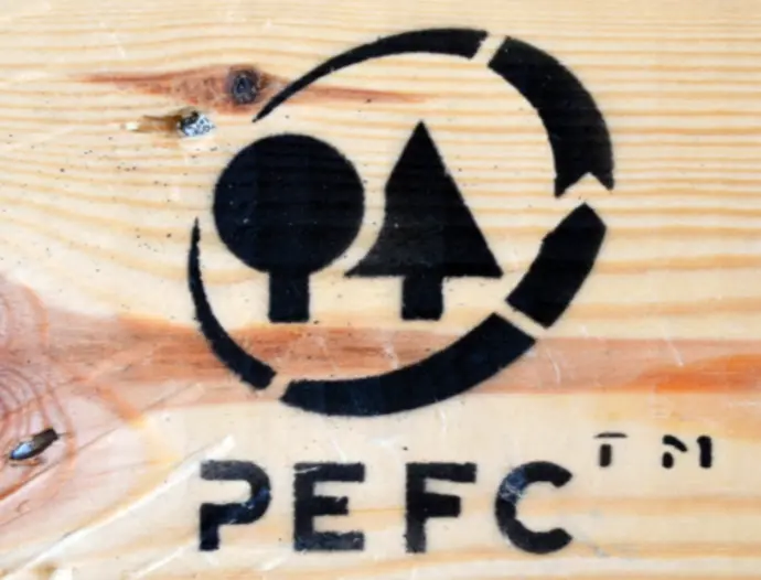 Le logo de PEFC, en noir, l'organisme de certification forestière sur un fond bois clair 